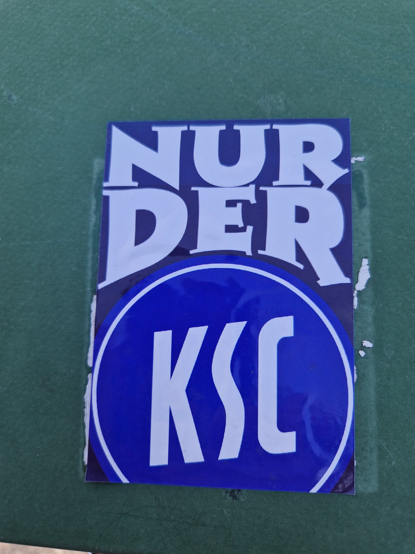 Close-up of a blue and white sticker with the text "Nur der KSC". The sticker features a circular logo with the letters "KSC" in white. The text "Nur der" is written above the logo in a stylized font.