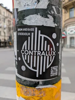 A black and white Contralux drum and bass sticker is affixed to a pole in Stockholm. The sticker features the band's name and logo, as well as a QR code.
