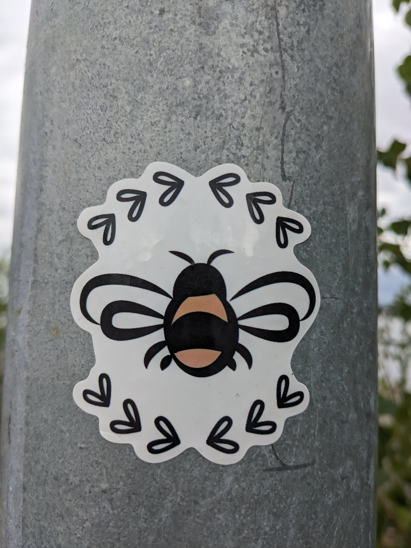 A cute bee sticker with a floral frame. The bee is black and peach in color, and the frame is made of small black hearts and arrows.