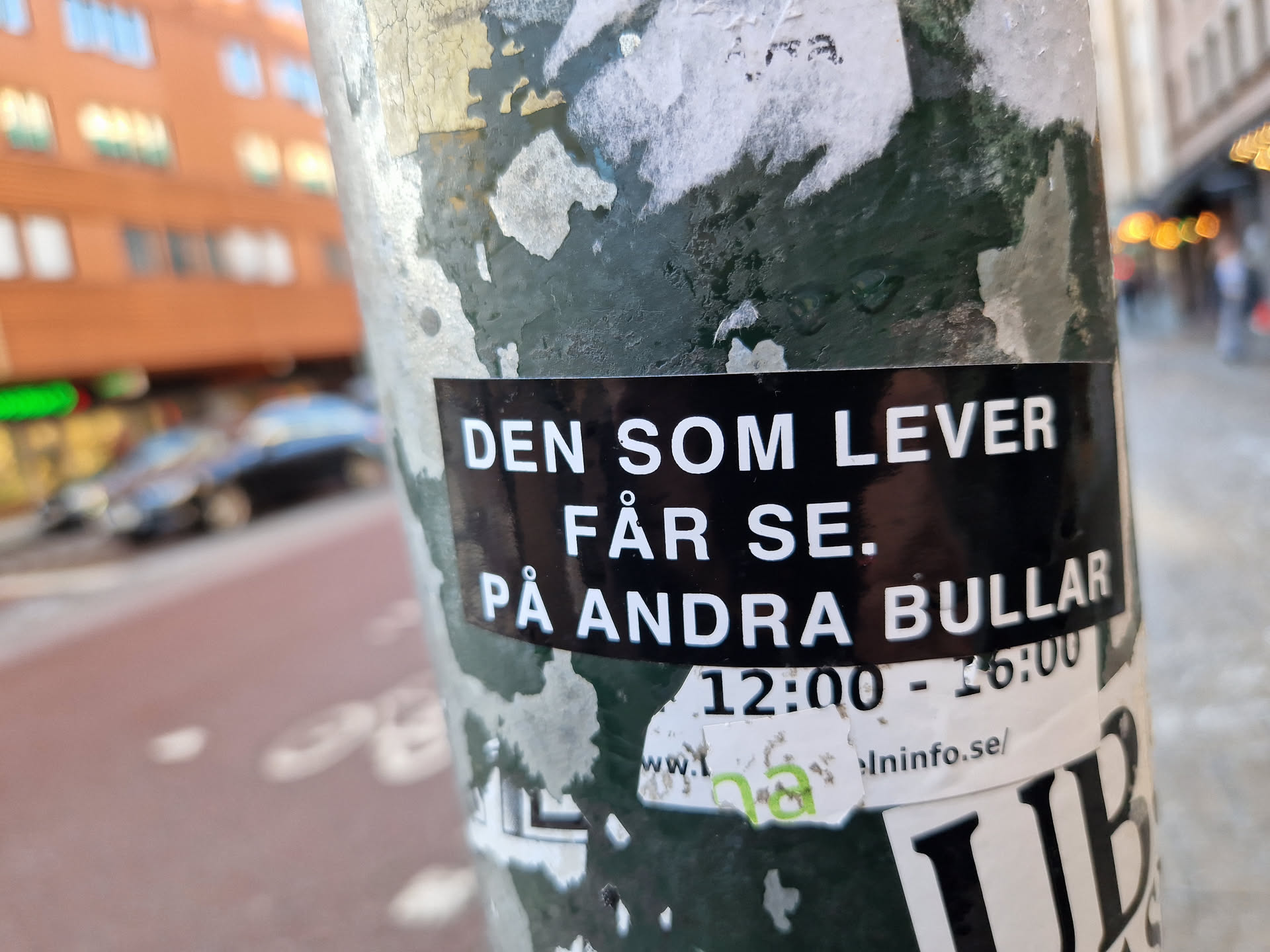 A sticker on a pole with Swedish text that translates to "He who lives will see. On other buns."  It also includes times 12:00 - 16:00 and a website address elninfo.se