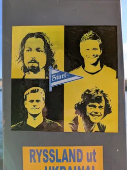 This sticker is divided into four quadrants, each containing a portrait in black and yellow. The top left shows a man with long hair and a beard, the top right features a man with short blond hair, the bottom left contains a man with short hair and the bottom right shows a man with curly hair. In the center, there is a blue and white pennant with the word "Start" written on it.