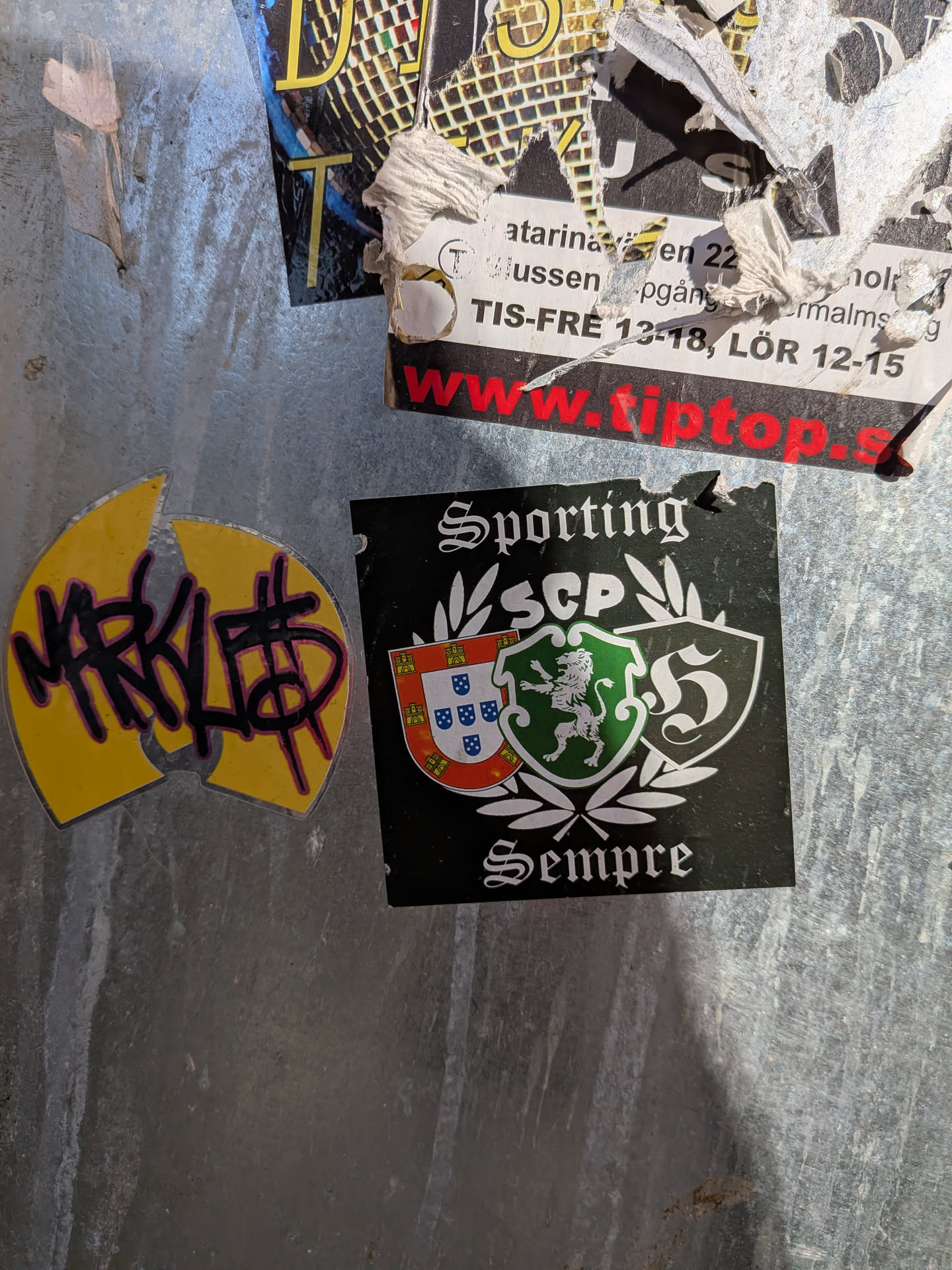 The central sticker is a square-shaped, predominantly black sticker. At the top, in a white gothic-style font, is the word "Sporting". Below this, the letters "SCP" (likely an acronym for Sporting Clube de Portugal) are displayed in white, flanked by white laurel wreaths. Further down, two shield-shaped crests are featured: the left one depicts the Portuguese national shield (red border with castles, white background with blue shields), and the right one is green with a white rampant lion, the emblem of Sporting CP. To the right of these crests is a stylized white 'S' within another shield outline. At the bottom, in the same gothic-style font, is the word "Sempre" (Portuguese for 'Always'). The sticker has a slightly worn top edge.