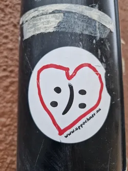 A round white sticker with a red hand-drawn heart containing a combination of a happy and sad face. The website www.uppochner.nu is written at the bottom of the sticker.