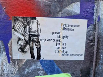 A sticker with an image of a person standing with a keffiyeh and the word PALESTINE vertically with other words. The text is a call for justice and the end of the occupation.