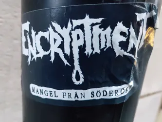 Street sticker Black and white sticker with the band name ENCRYPTMENT in a stylized font. Below the name is a small drawing of a noose and the text "MANGEL FRÅN SÖDERÖK" (lack from Södermalm).