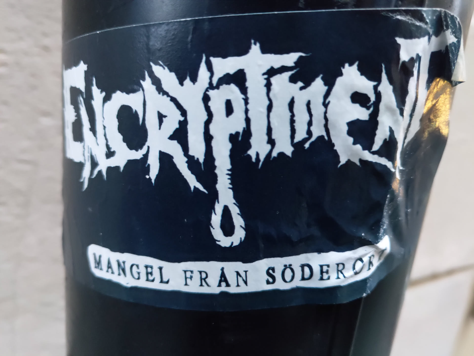 Black and white sticker with the band name ENCRYPTMENT in a stylized font. Below the name is a small drawing of a noose and the text "MANGEL FRÅN SÖDERÖK" (lack from Södermalm).