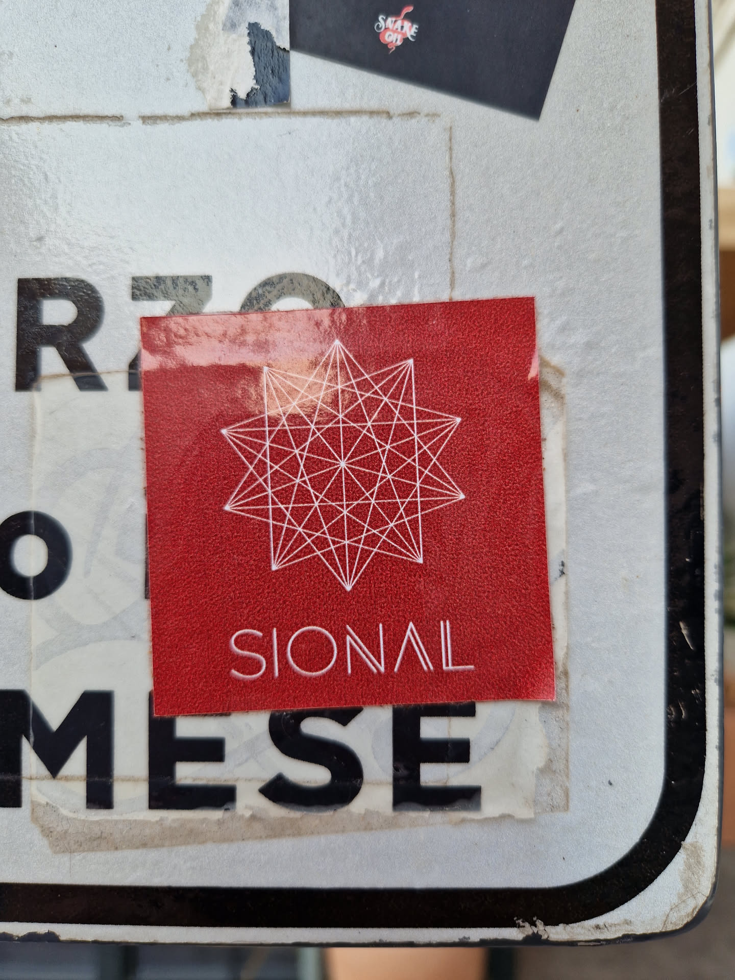 A red square sticker with a white geometric design resembling a star. The word SIONAL is printed in white beneath the design.