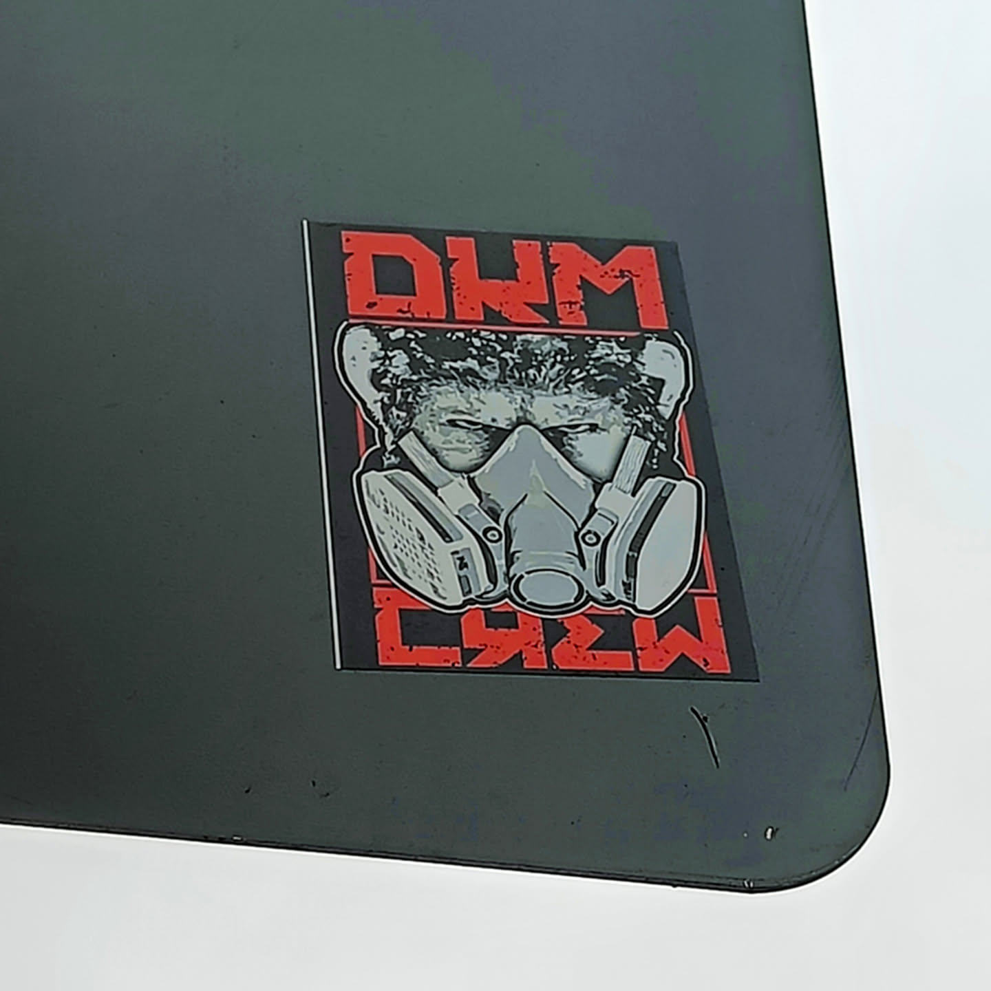 A sticker featuring a grayscale image of a person wearing a gas mask, with the text "DM CREW" in red on a black background.
