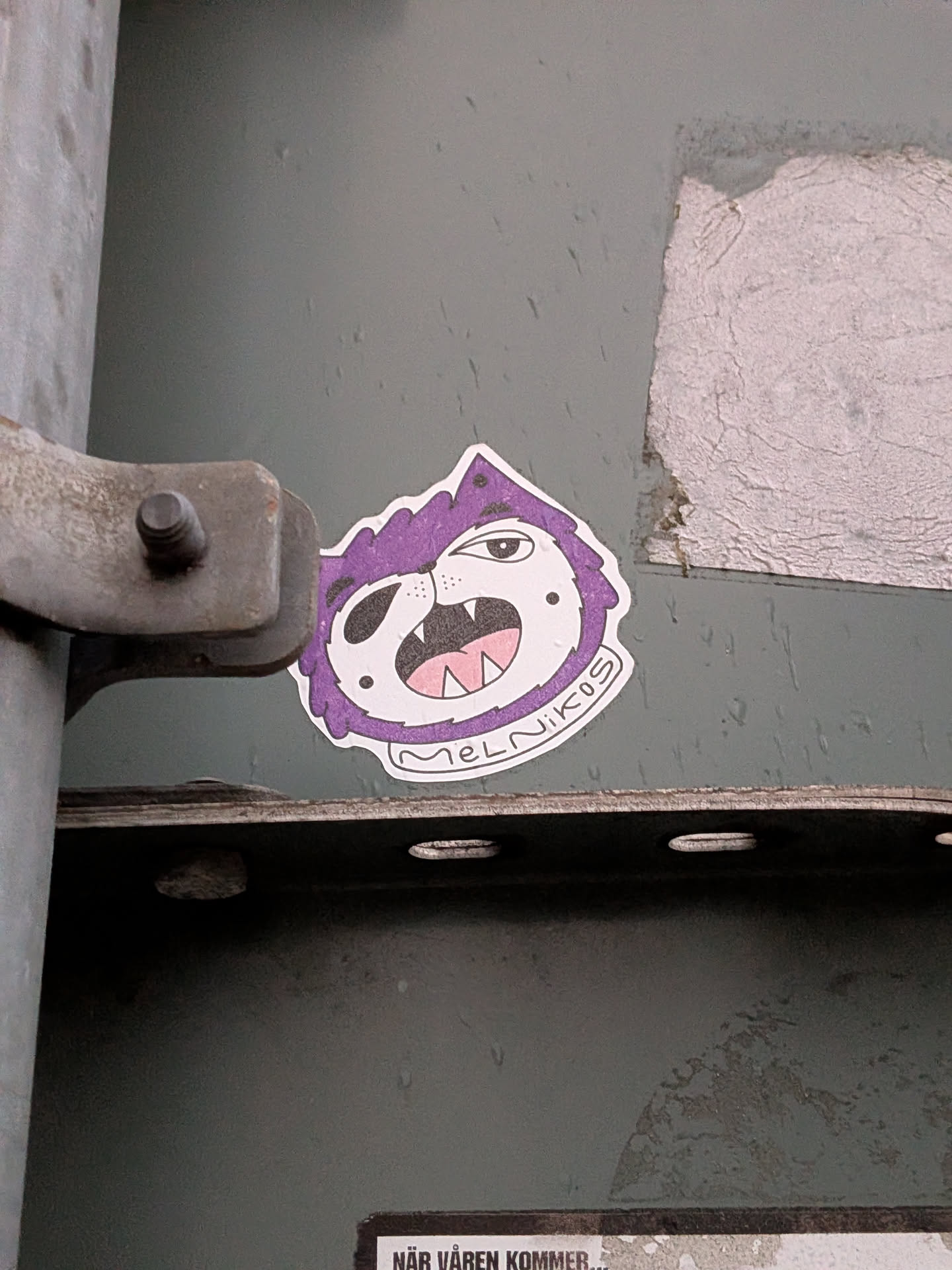 The sticker features a cartoonish monster's head with a purple, spiky mane. The monster has a white face with a black eyepatch covering its left eye. Its right eye is open and looking forward. It has a wide-open mouth revealing sharp white teeth and a pink tongue. The outline of the sticker is irregular, following the shape of the monster's head and mane. Below the mouth, in a white arc, is the text 'MELNIKOS'. The sticker has a white border.