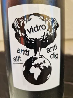 Black and white sticker with a drawing of a mushroom cloud over a globe. The text Vidro is in the cloud, and the text Anti-allt Anti-dig is below the globe.