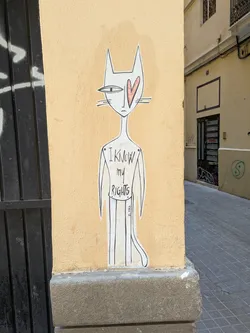 A white, stylized cat sticker affixed to a yellow wall. The cat has a slender body, thin limbs, and large pointed ears. One of its eyes is a solid red heart. Text on the body reads "I know my rights" in all caps. The signature "C.SKA" is visible at the bottom right of the sticker.