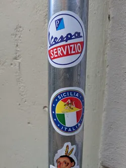 A round sticker features the flag of Sicily, Italy, with a Trinacria symbol in the center. The flag is split diagonally into yellow, red, and green sections. The sticker is surrounded by a blue border with white stars and the words "SICILIA" and "ITALIA".
