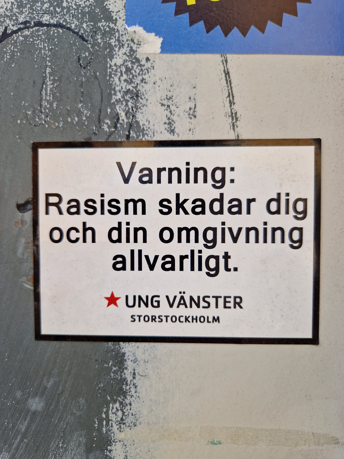 A sticker warning against racism.  It's in Swedish and states that racism seriously harms you and those around you.  The sticker is from Ung Vänster Storstockholm (Young Left Stockholm).