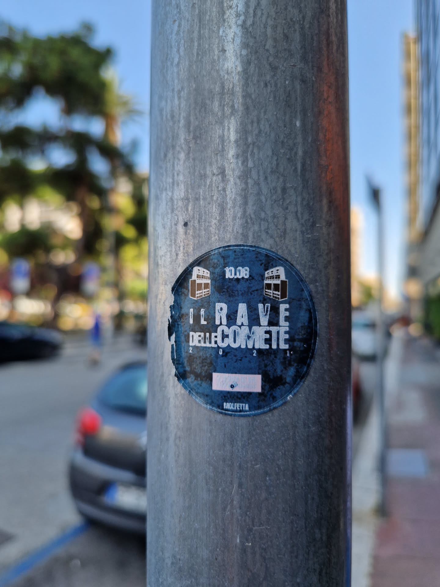 A sticker featuring the text "Il Rave delle Comete" (The Comet Rave) and the date 10.06.  The design is round and dark blue with white text and small images. It's affixed to a metal pole.
