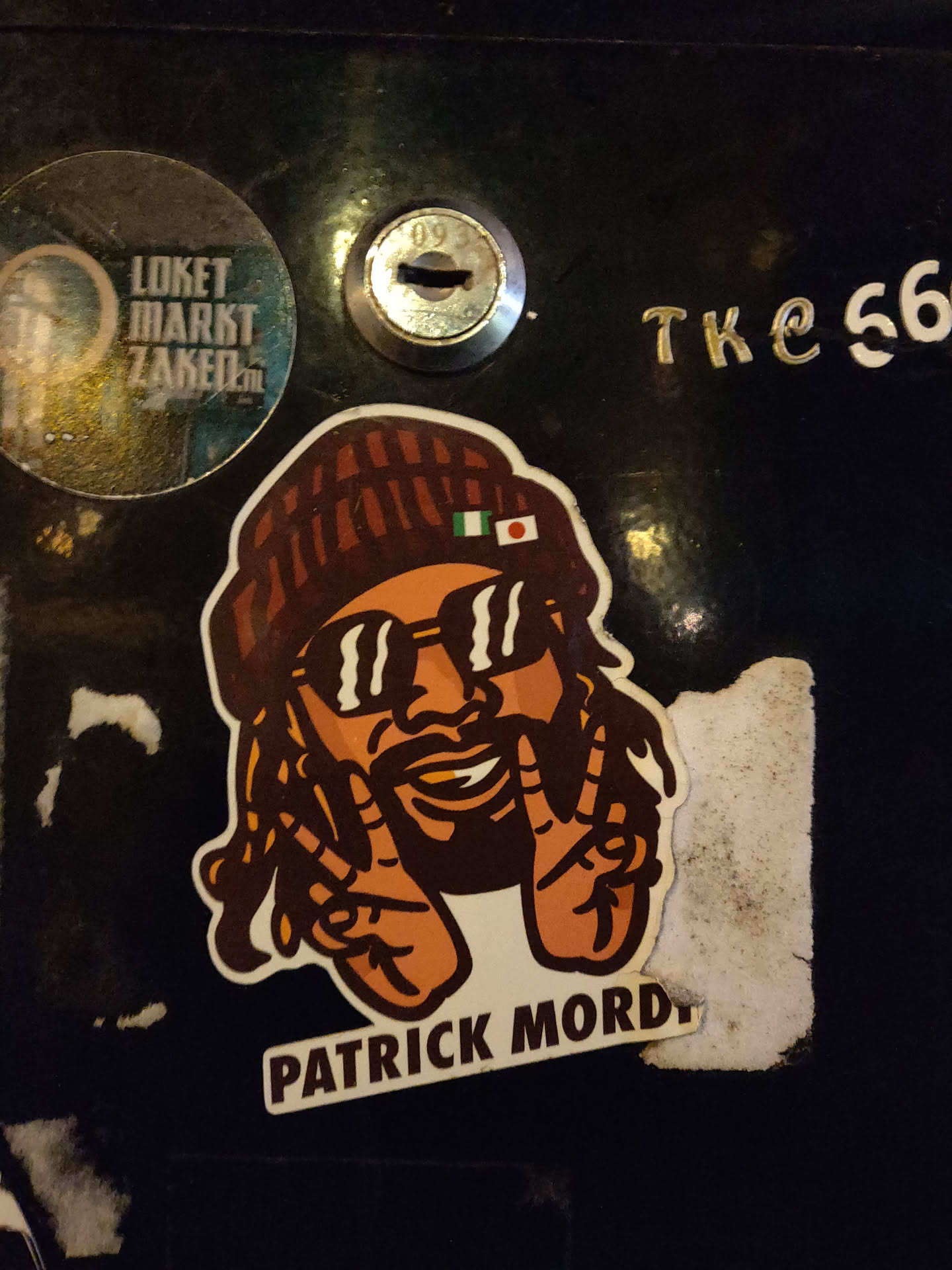 A sticker featuring an illustration of Patrick Mordy, a person with dreadlocks wearing a beanie and sunglasses, making a peace sign with both hands. The beanie has the Nigerian flag on it. 