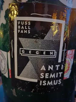 A black and white sticker with the text "Fussball Fans gegen Antisemitismus" (Football Fans against Antisemitism) in German. The design includes a geometric shape.