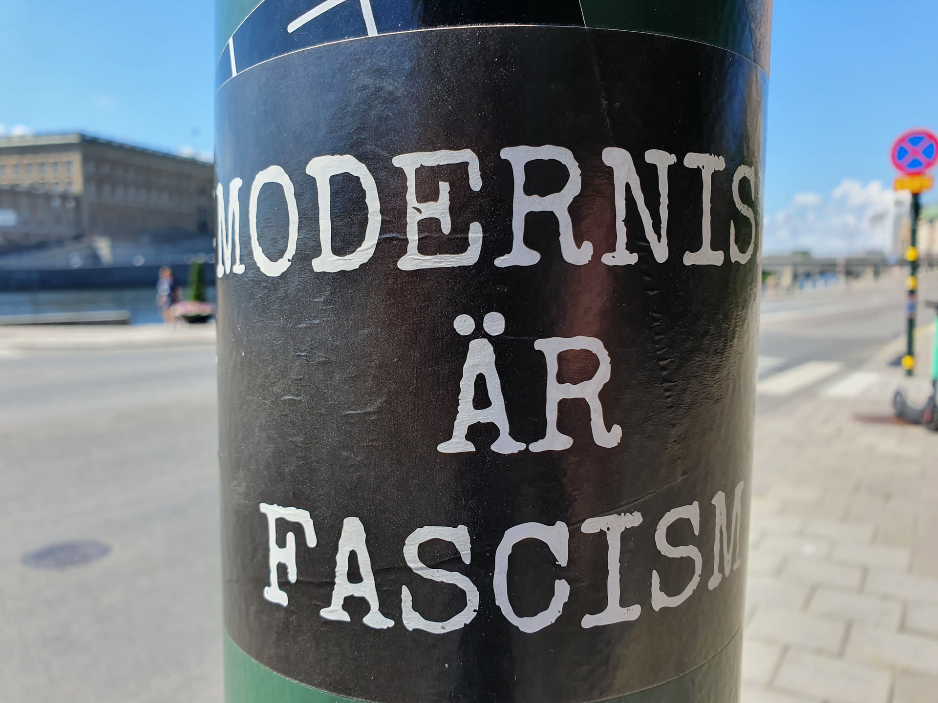 A black sticker with white text on a pole. The text says "Modernism är Fascism" in a typewriter-style font.