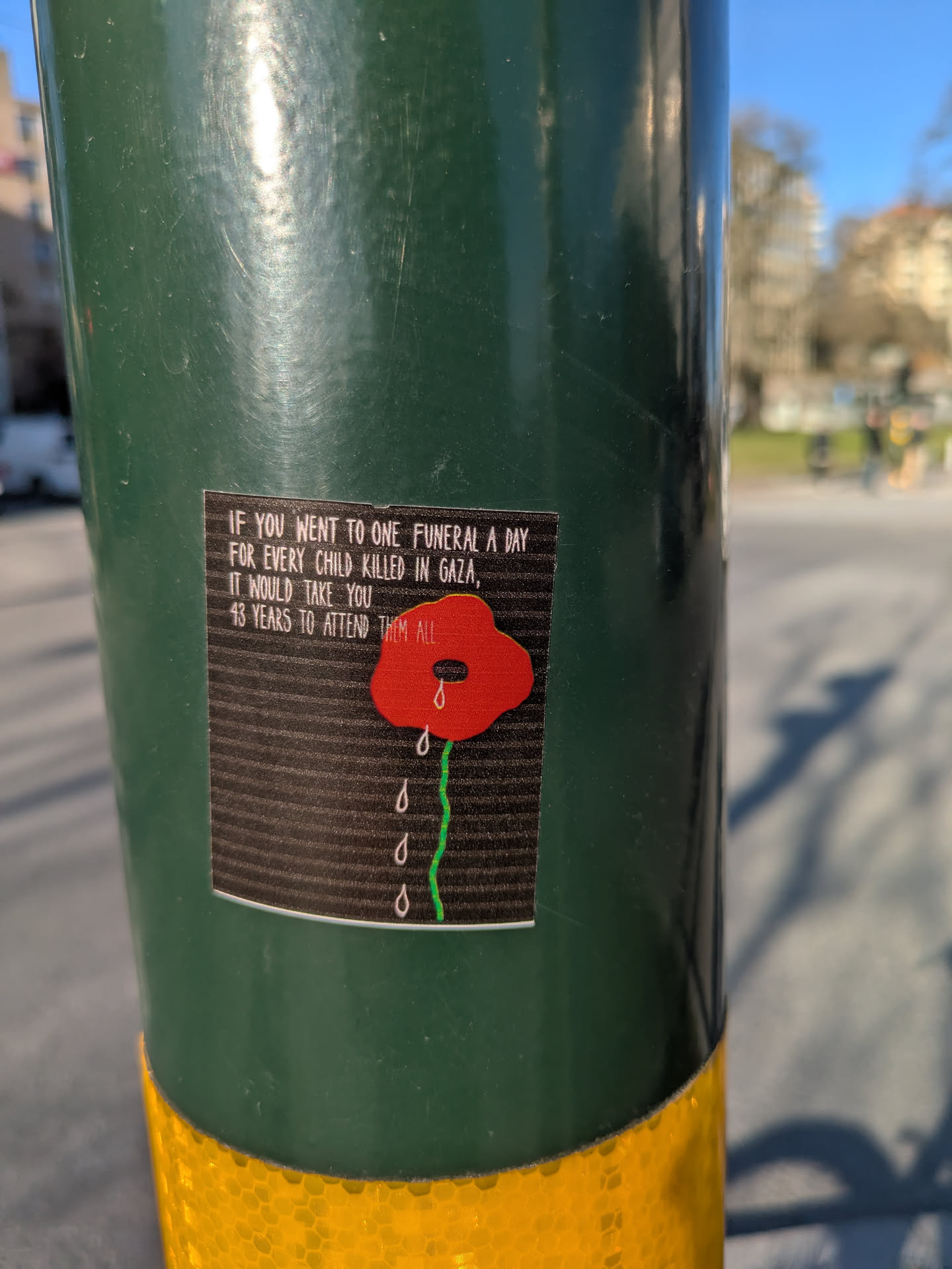 The sticker features a red poppy with teardrops beneath it, symbolizing mourning, with the text 'IF YOU WENT TO ONE FUNERAL A DAY FOR EVERY CHILD KILLED IN GAZA, IT WOULD TAKE YOU 13 YEARS TO ATTEND THEM ALL.'