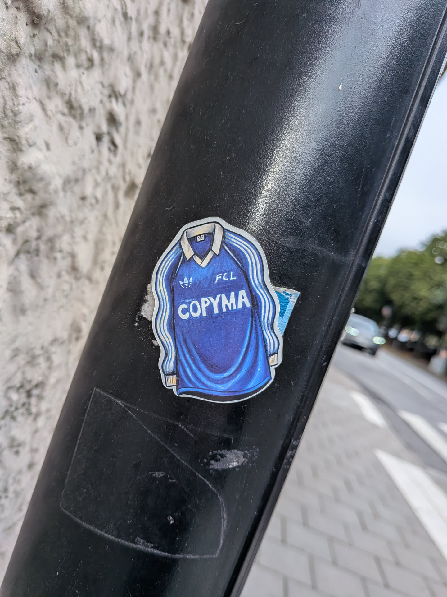 A die-cut sticker depicting a classic blue long-sleeved football jersey with a white collar. The jersey features three white stripes down the sleeves, an Adidas trefoil logo on the right chest, 'FCL' on the left chest, and the sponsor name 'COPYMA' printed in large white letters across the center. The illustration has a textured, hand-drawn appearance.