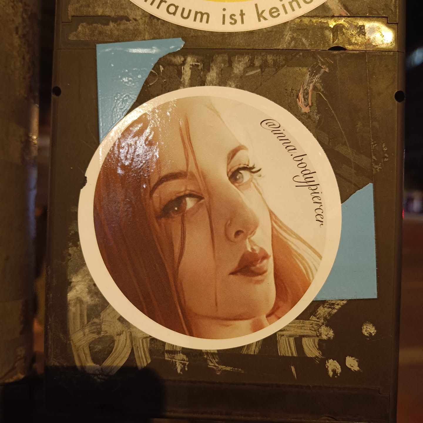 Round sticker featuring a stylized illustration of a woman with long brown hair.  The art style is slightly painterly, with visible brushstrokes. The woman is looking off to the side with a subtle, pensive expression. The sticker includes the Instagram handle @inna.bodypiercer.