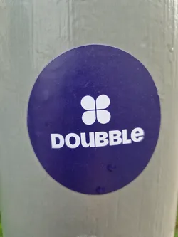 Round purple sticker with a white four-leaf clover and the word DOUBBLE in white uppercase letters.  The sticker is affixed to a light gray pole.