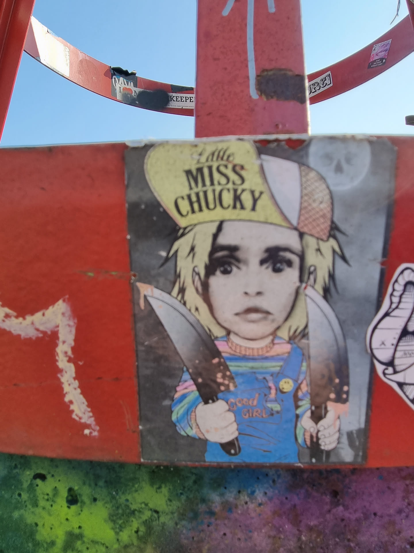 Sticker depicting a stylized Chucky doll from the Child's Play franchise, holding two knives. The doll is wearing a yellow hat with the text "Little Miss Chucky" on it. The sticker has a dark and slightly gritty aesthetic.