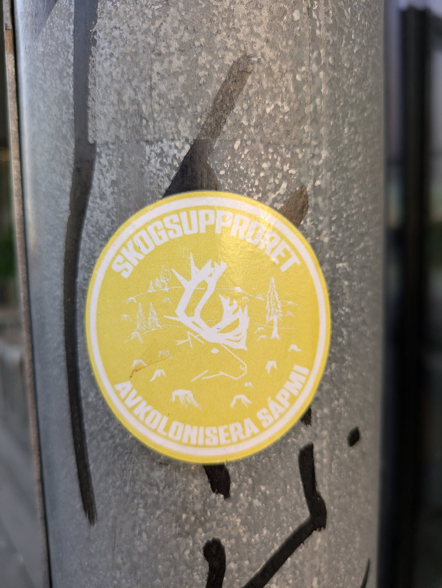 Yellow round sticker with a reindeer illustration and text in Swedish.  The text translates to "Forest Uprising: Decolonize Sapmi".