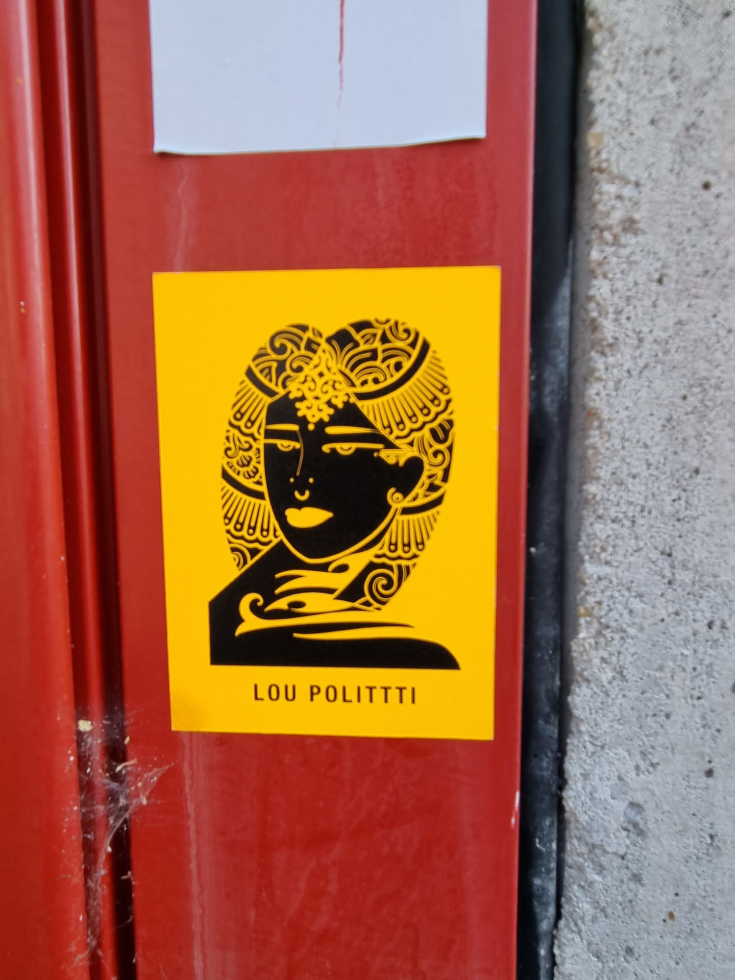 Yellow sticker with a black illustration of a woman's face adorned with intricate headwear. The artist's name, LOU POLITTI, is printed at the bottom. 