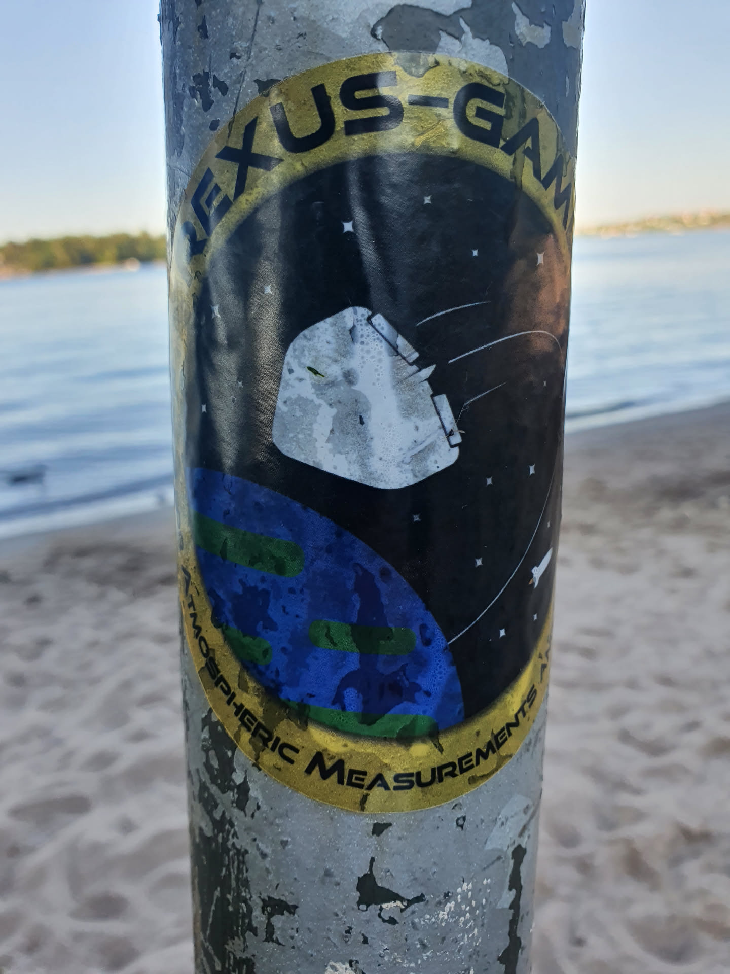 A sticker featuring a design resembling a space mission patch.  It shows a spacecraft orbiting a stylized Earth against a dark background. The text 'NEXUS-GAM Atmospheric Measurements' is prominently displayed in a circular band around the main image.