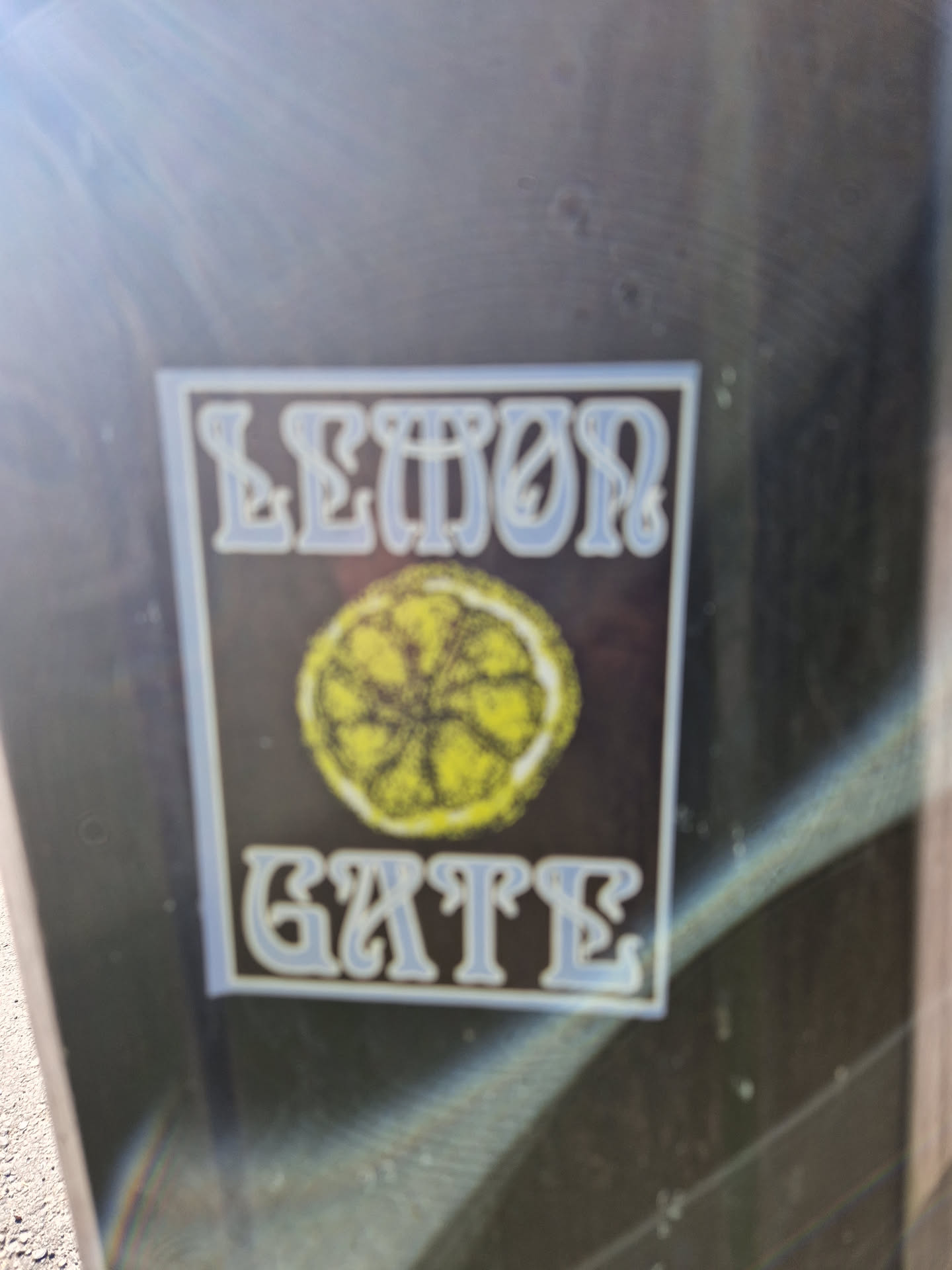 A sticker with the words "Lemon Gate" in a stylized font, accompanied by a graphic of a lemon slice. The sticker has a black background with light blue text.