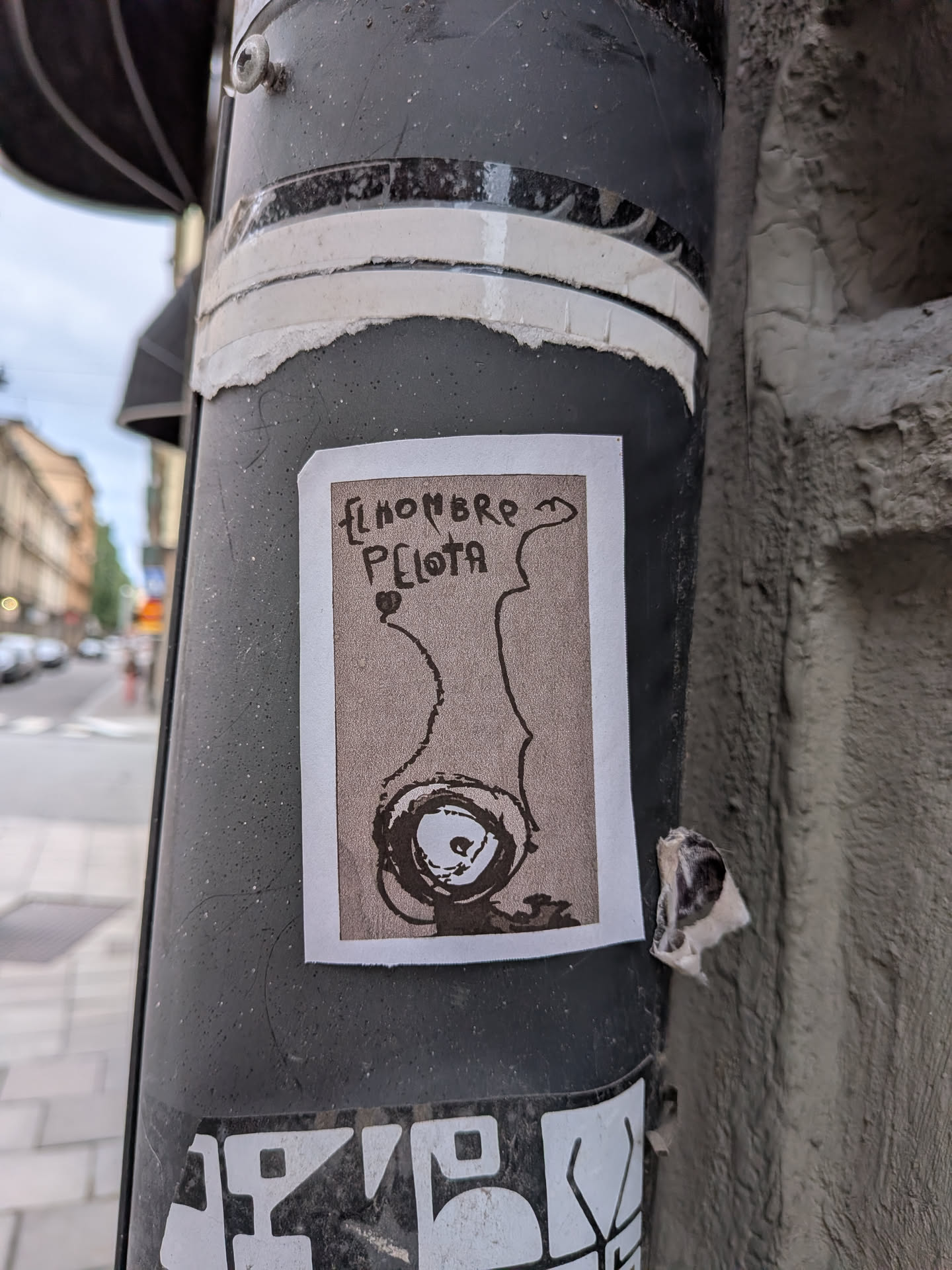 Rectangular sticker with a white border and beige background. It displays a black ink drawing of an abstract, eye-like circular figure with wavy lines extending upwards, accompanied by hand-written Spanish text at the top.