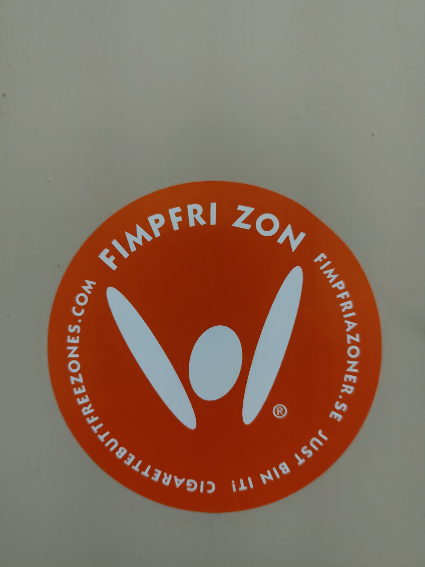Orange circular sticker with a logo and text indicating a cigarette bin and a website. The logo depicts a stylized figure with raised arms.