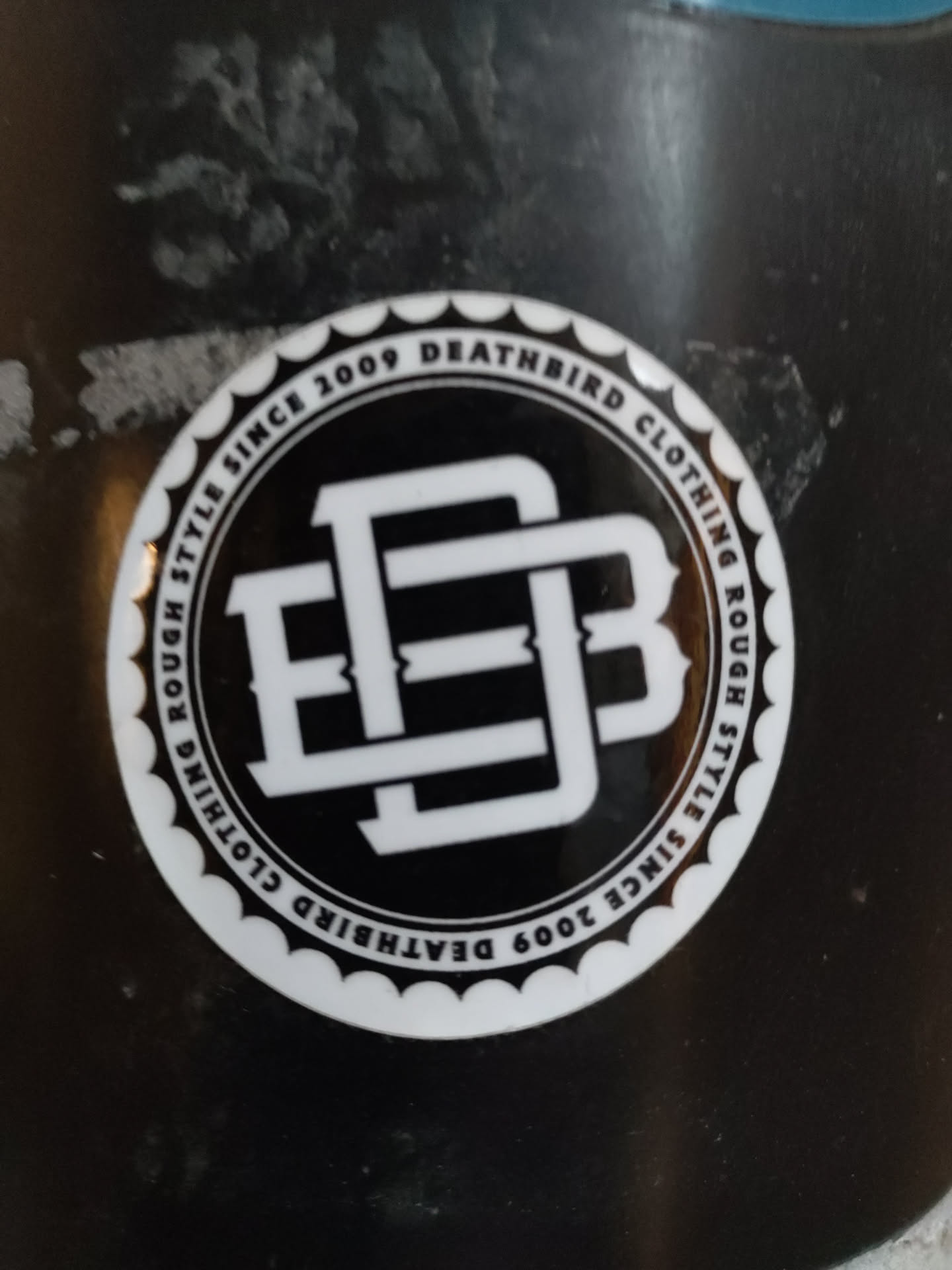 Circular sticker with the Deathbird Clothing logo. The logo is a monogram of the letters DB in a bold, stylized font.  The text around the logo says "Rough Style Since 2009 Deathbird Clothing".