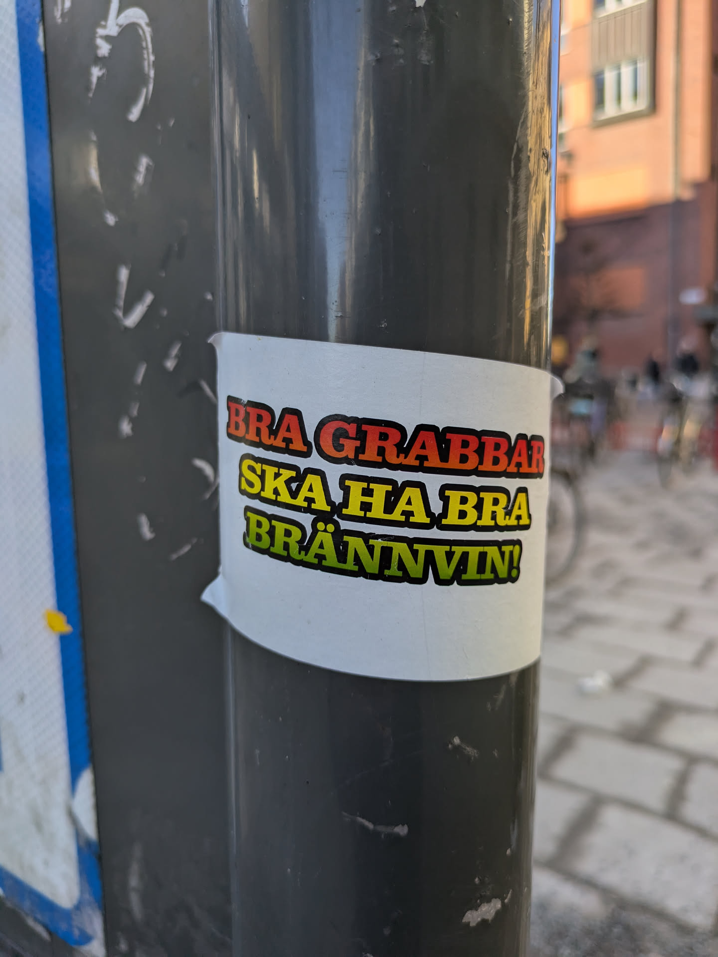 A sticker on a pole with Swedish text that reads "BRA GRABBAR SKA HA BRA BRÄNNVIN!", which translates to "GOOD GUYS SHOULD HAVE GOOD BOOZE!"
