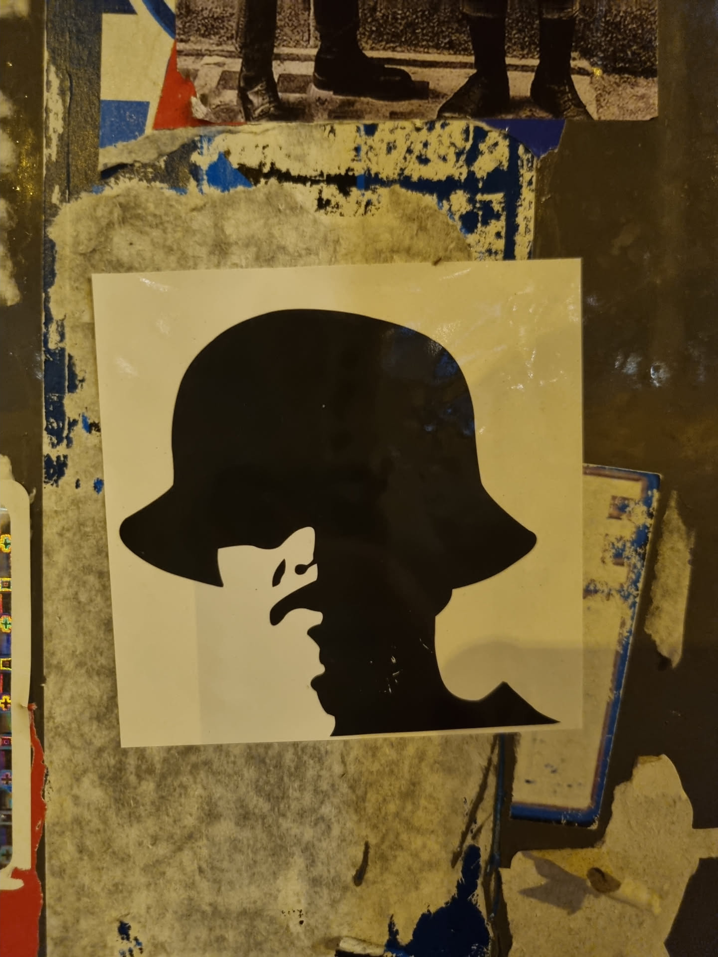A black and white sticker featuring a stylized profile of a person wearing a wide-brimmed hat.  Half of the face is in shadow, creating a sense of mystery. The art style is simple and graphic.
