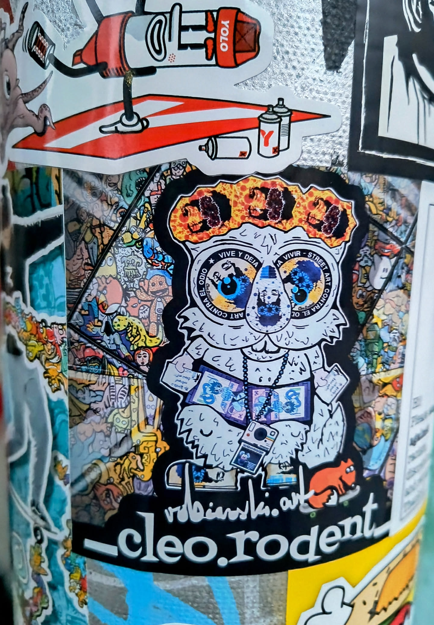 A sticker featuring a cute cartoon rodent character with large eyes. The character is wearing a necklace with the word 'STARS' and holding a camera. The sticker has a black background with the artist's name and website address at the bottom.