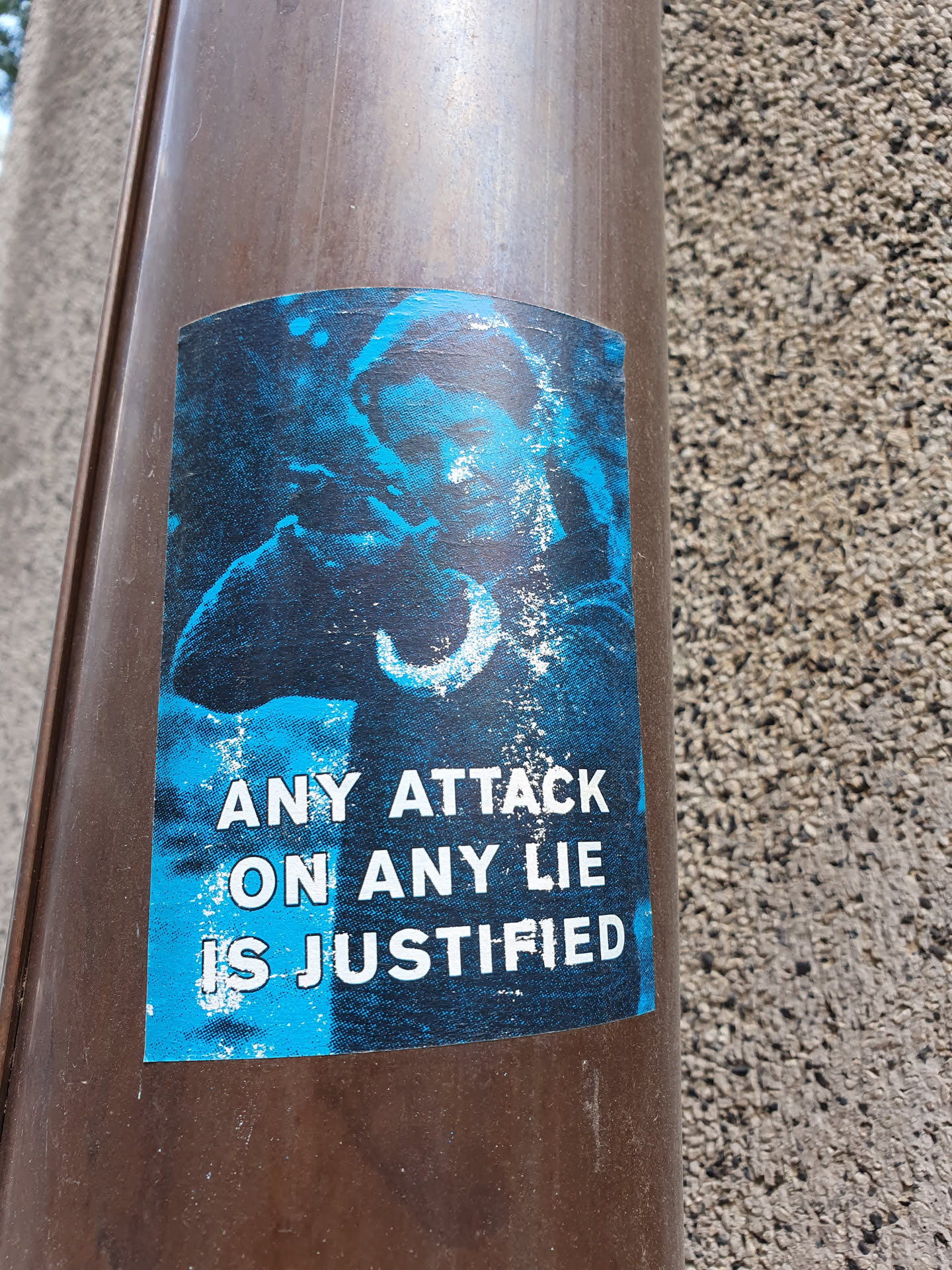 A blue sticker with a picture and a phrase on it. The phrase says: Any attack on any lie is justified.