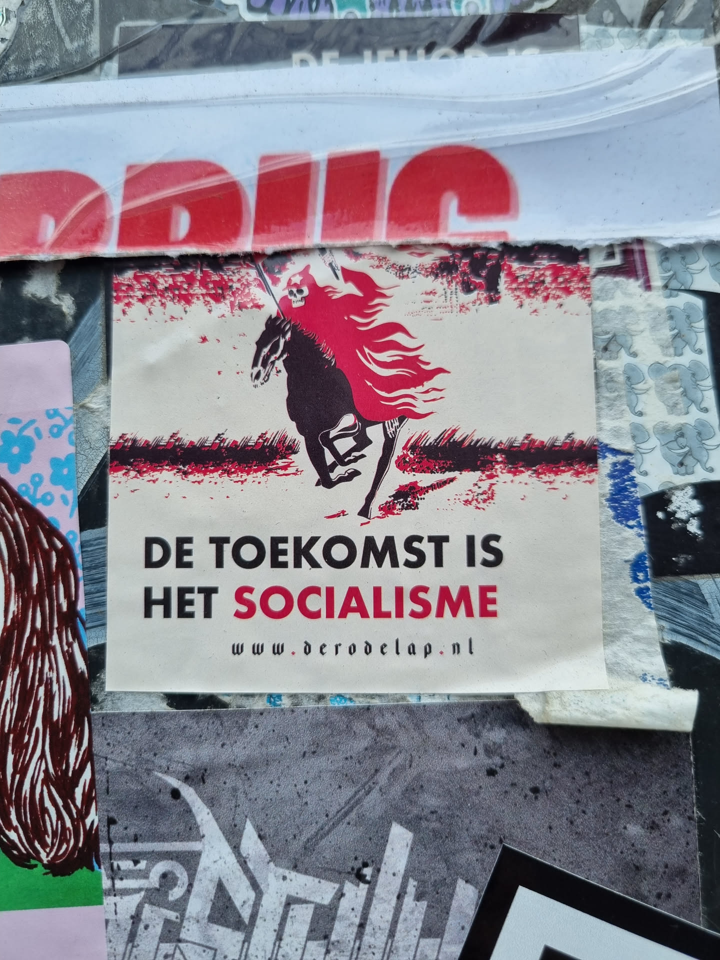 A sticker with a design depicting a figure on horseback, with flames for a cape. The text on the sticker says: "De toekomst is het socialisme" (The future is socialism) and includes a website: www.derodelap.nl