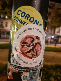 A sticker featuring a pomegranate with the text "MENSTRUATION #TIREDME @LAIASFETABALANCE OWN YOUR MENSTRUAL CYCLE".  There is a QR code on the sticker.