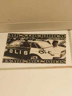 A sticker depicting a black and white image of a police car with graffiti on it. The text on the sticker says "AIR STOCKHOLM" at the top and "ENADE MOT POLIS" at the bottom.  The word POLIS is visible on the car itself. The image appears to be from a demonstration or protest.