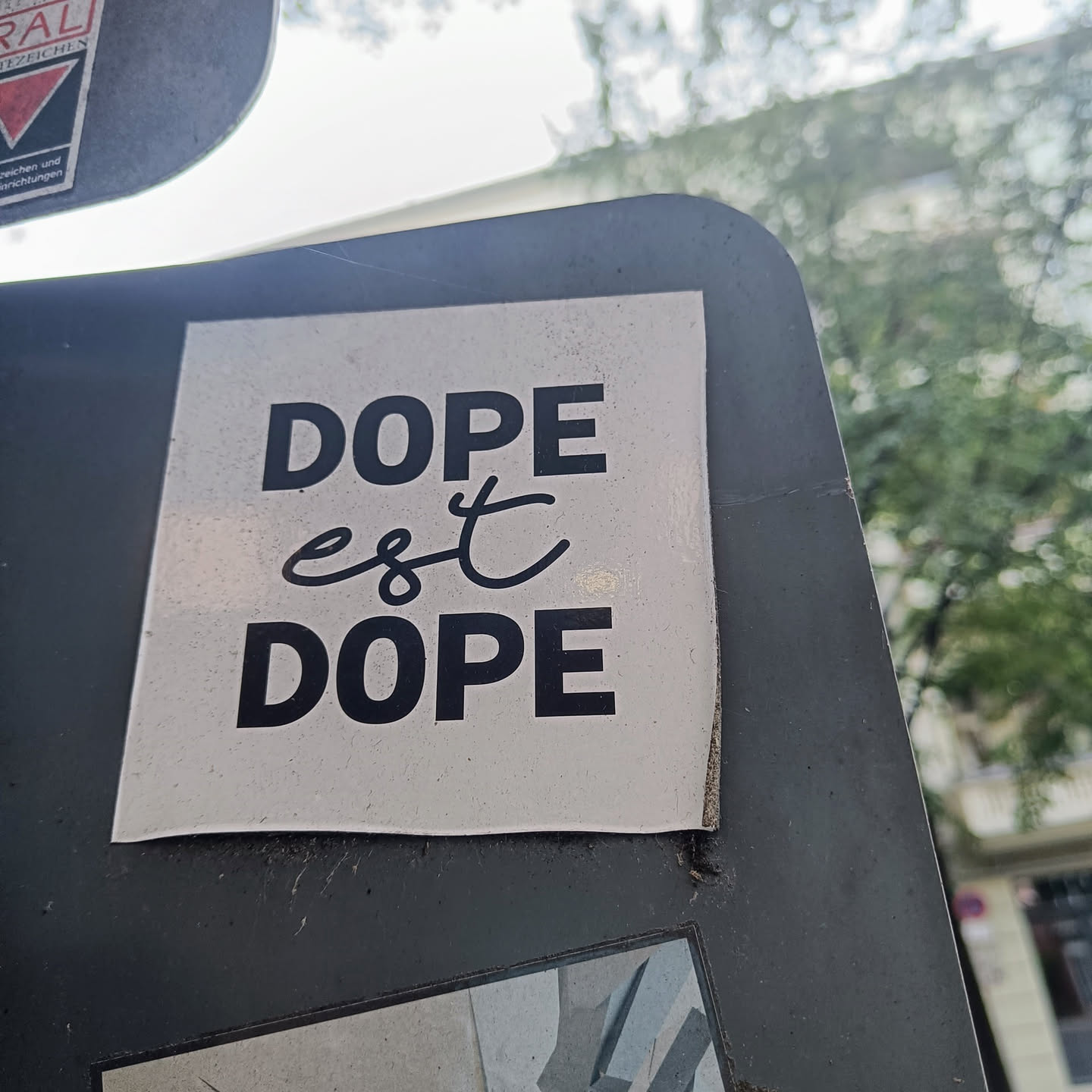 A sticker with the text "Dope est Dope" in black on a white background. The word "est" is written in a cursive style.
