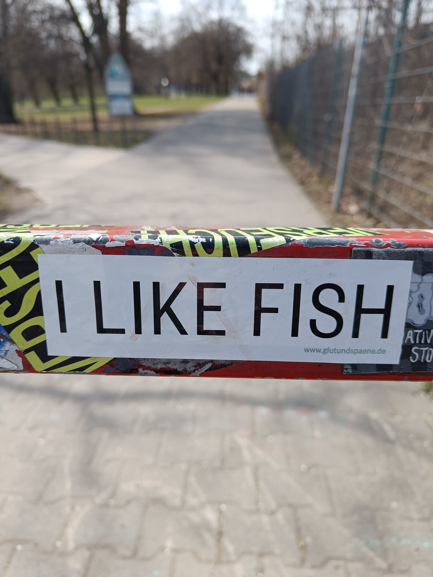 A simple sticker with the text "I like fish" on it. It is placed on a pole with other stickers.