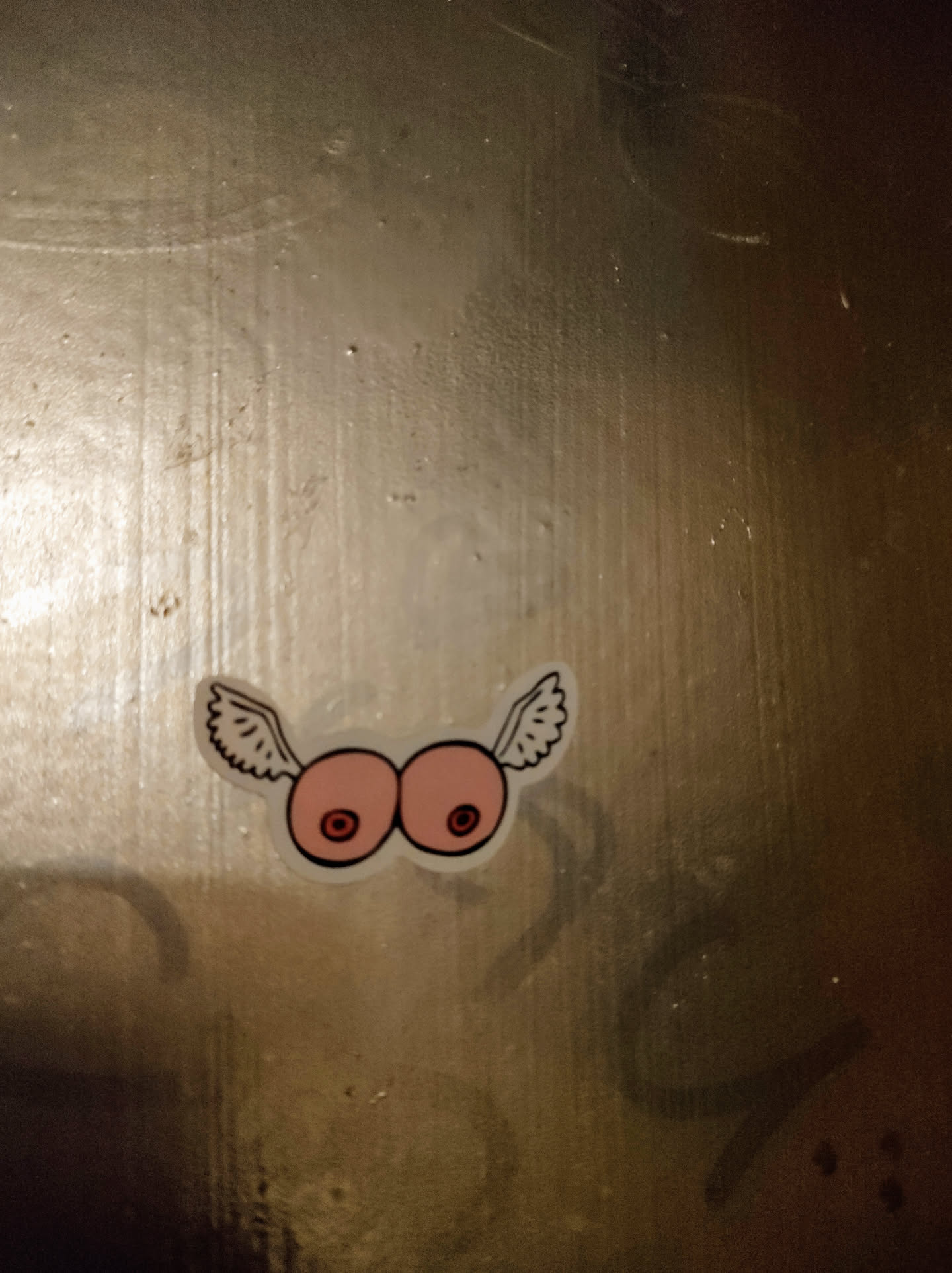 A sticker depicting a pair of breasts with wings.  The style is simple and cartoonish.
