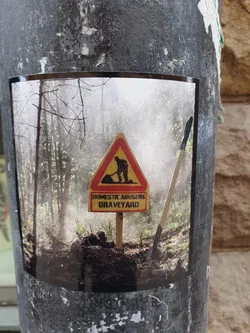 A sticker depicting a sign that reads 'Domestic Abusers Graveyard' in a forest setting.  The sign is similar to a construction or road work sign, with a figure shown digging a grave.
