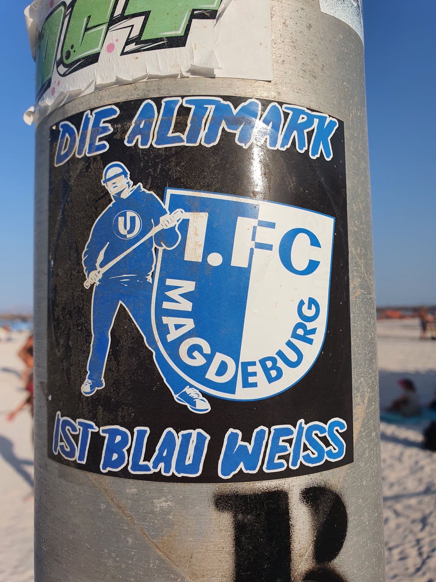 A sticker featuring a stylized illustration of a person holding a cleaning tool, possibly a brush or broom, in front of a logo that appears to be for 1. FC Magdeburg. The text 'DIE ALTMARK IST BLAU WEISS' is prominently displayed, which translates from German to "The Altmark is blue and white."