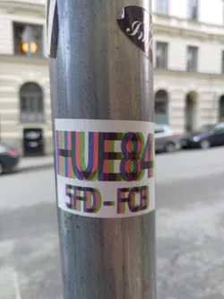 A colorful sticker with the text HUE84 and 5FD-FCB. The text is stylized with overlapping letters in various colors.