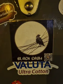 A sticker featuring a black crow perched on a network of lines within a circular design.  Below the crow image, the text "BLACK CROW" is visible, followed by the brand name "VALUTA" and the description "Ultra Cotton". A QR code is also present on the sticker.