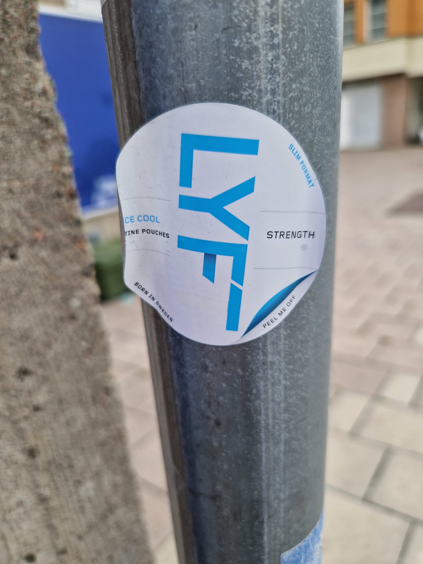 A round sticker with the LYF logo and text that says "Ice Cool, Cooling Pouches", "Slim Format", and "Strength". The sticker is attached to a metal pole.