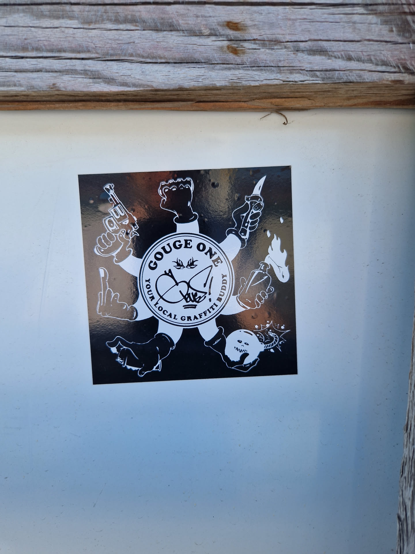 A black and white sticker featuring a central circular logo that says "Gouge One: Your Local Graffiti Buddy."  Surrounding the logo are various illustrations of hands holding weapons (guns, knives), a Molotov cocktail, and a bomb. The style is graphic and bold.