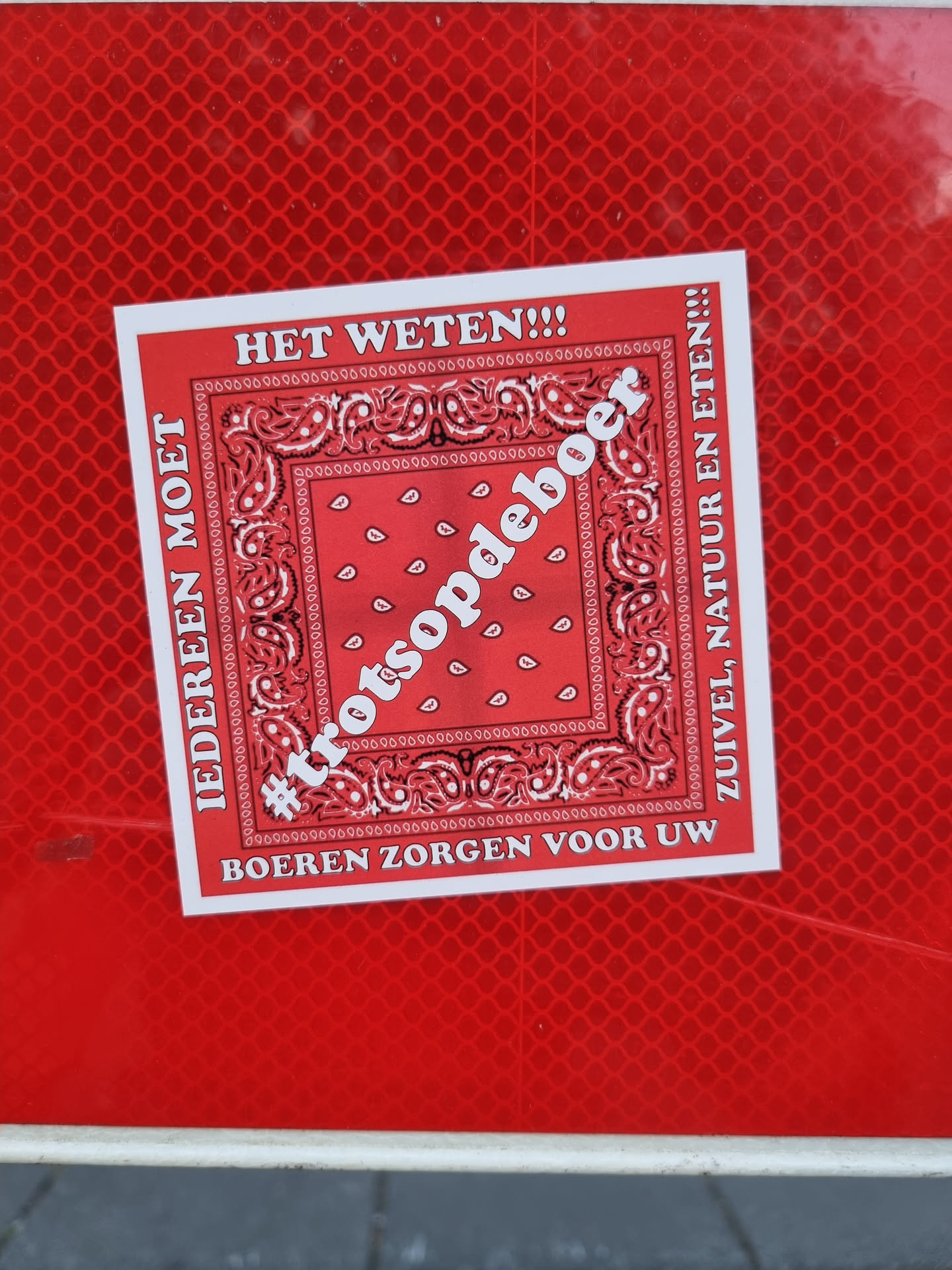 A red sticker with a bandana-like design and the text '#trotsopdeboer' (proud of the farmer) in the center.  The text around it translates to: Everyone must know!!! Farmers provide your dairy, nature and food!!!